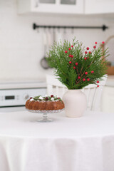 Christmas home interior in white kitchen-Christmas chocolate bundt cake with fresh berries and rosemary. Winter baking at Christmas. Ceramic vase with spruces brunches..