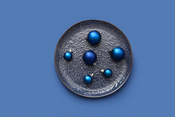 Plate with Christmas balls on blue background