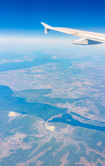 Naklejka premium Aerial view from airplane window above green ground. View from the airplane window with beautiful clouds at sunrise