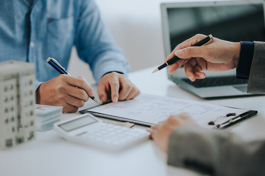 Close-up photo of a real estate agent offering a contract to purchase or rent a residence. Businessman holds small house model with property insurance at table in home sales office