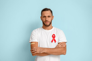 Young man with red ribbon and crossed arms on blue background. AID awareness concept - obrazy, fototapety, plakaty