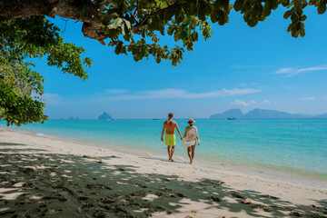 the backside of a couple of men and women sitting at the beach of Koh Kradan island in Thailand