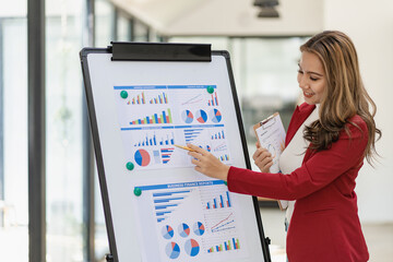 Asian female employee working using laptop computer at desk calculating expenses, financial reports on graph data sheet in office