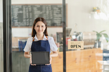 A young Asian female entrepreneur hangs a welcome sign in front of a food and beverage shop. A beautiful waitress holds a tablet and prepares instructions for ordering food in the restaurant.