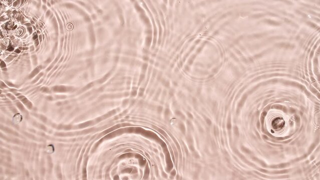 Pure pink water with reflections sunlight slow motion of drop falls into water and diverging circles of water. Sun and shadows. Water drop splash blue colored. 4k. High quality 4k footage