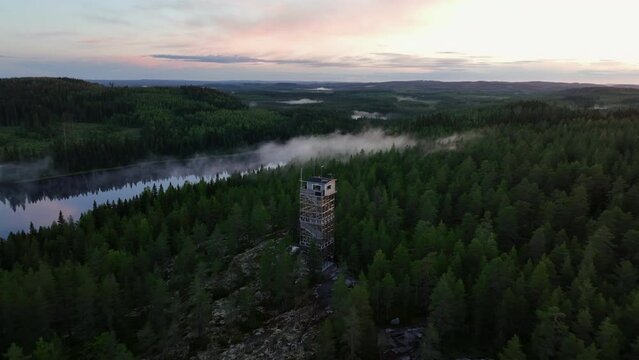 Aerial pull back from a watchtower, in middle of nordic, foggy sunrise forest