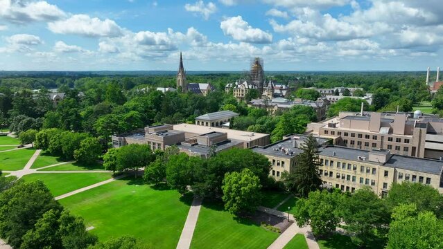 University of Notre Dame campus on beautiful summer day. Aerial descending shot above green lawn with Basilica of the Sacred Heart steeple and Main building golden dome.