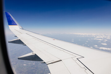 Obraz premium Beautiful view from the airplane window from above to the clouds, mountains, roads, rivers. Picturesque landscape from a helicopter window. Airplane wing in the window above the clouds on a sunny day.