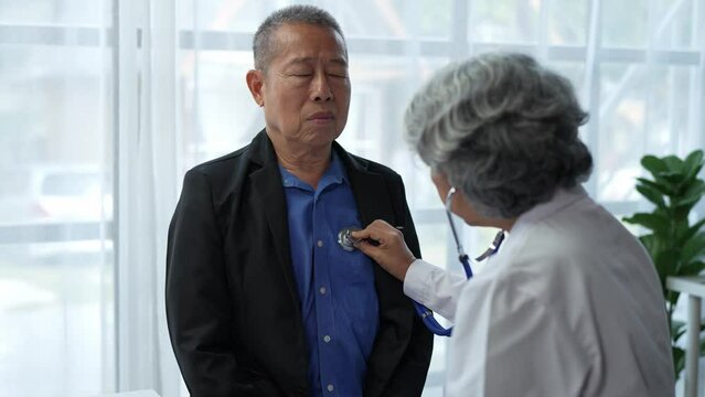 A female specialist doctor with a stethoscope listens to the lung and heart sounds of an elderly male patient doing a health check at the clinic or in the hospital. Concept of care, health insurance.