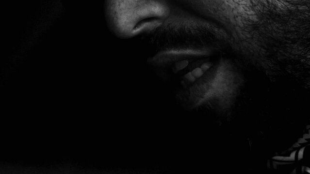 monochromatic close up footage of a bearded man smoking a cigarette and blowing smoke in the air.