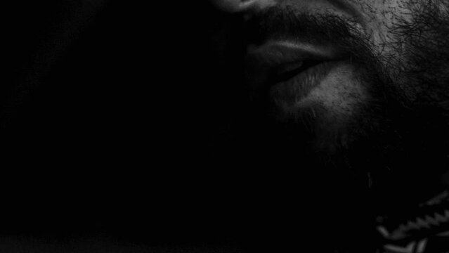 monochromatic close-up footage of a bearded man smoking a joint or cigarette with dense smoke in the air.