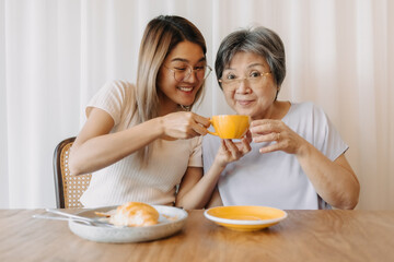Obraz na płótnie Canvas Happy Asian old woman mother and adult daughter eating croissant bakery and drinking coffee tea at cafe, holding cup and spending happy life time together over white curtain.