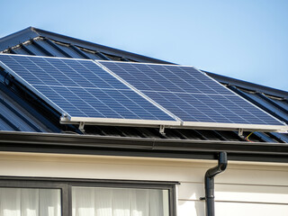 Solar panels on concrete tile roof of residential house with white wooden plank walls.
