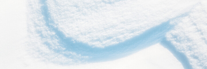 Wide panoramic winter background with snowy ground. Natural snow texture. Wind sculpted patterns on snow surface. Closeup top view with copy space.