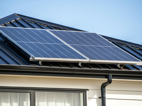 Solar panels on concrete tile roof of residential house with white wooden plank walls.