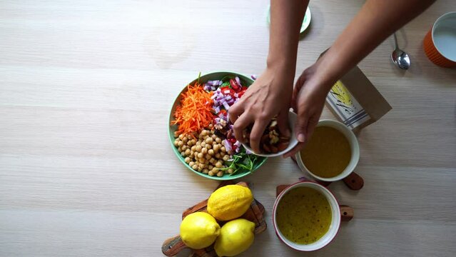 Aerial shot making of a salad adding tomatoes carrots spinach chick pease lemons onions nuts dressing in view