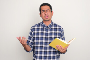 Adult Asian man holding a book with confused expression