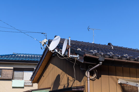 住宅の屋根に設置されたテレビ放送の衛星放送受信用アンテナと地上波受信用アンテナ