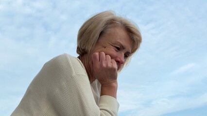 adult elderly woman is sad and thinks about life on the balcony against the sky 