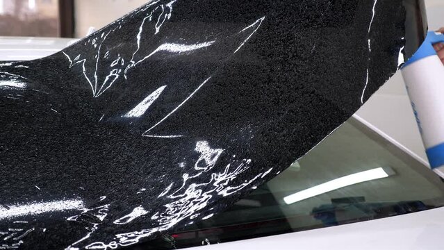 A close-up of a car service master splashing water on the glass before gluing tinted film in an auto repair shop. The process of tinting the car.