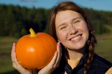 Happy young woman in nature, countryside with pumpkin, concept autumn, harvest, village, halloween