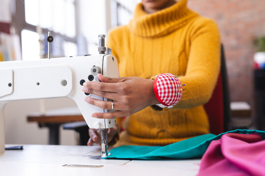 Biracial female fashion designer using sewing machine in sunny studio