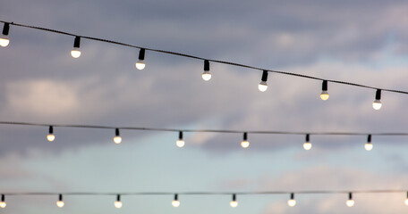 Festive light bulbs shine against the background of the sky with clouds