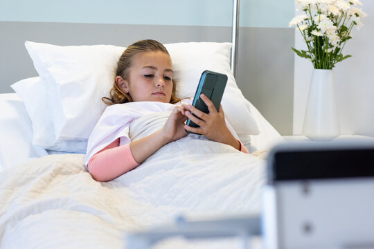 Caucasian girl patient lying in hospital bed using smartphone