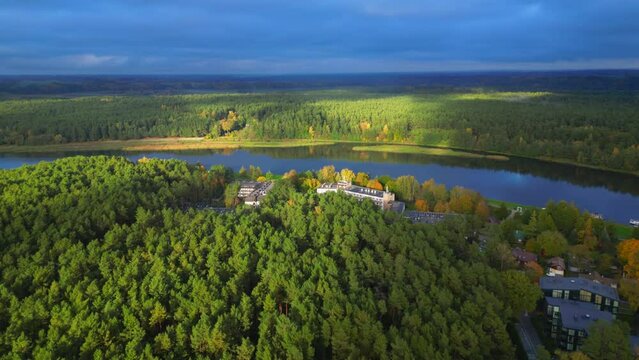 Autumn forest in sunlight with dark clouds next to river in tradition Lithuanian village