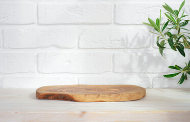 Wooden podium on table with green plant leaves and white brick wall background