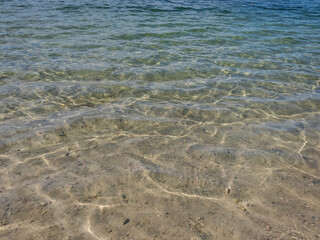 Crystal clear transparent water in shades of blue and turquoise with fine white sand base with bright reflection of sun in water movement