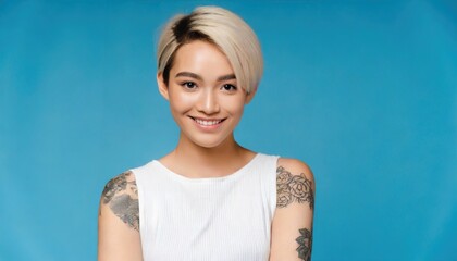 Fototapeta premium Smiling blond pretty smiling girl beauty female gen z model with short blonde hair beautiful face healthy skin and tattoo looking at camera wearing white top isolated at blue background