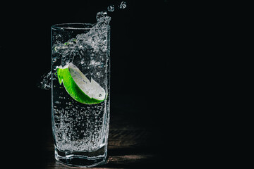 Gin tonic cocktail with lime slice in a glass splash on black background