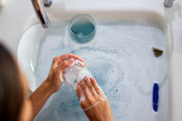 woman hands, cleaning dishes and water in sink in kitchen for clean home morning routine. Bacteria,...