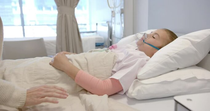 Midsection of caucasian mother holding hand of daughter patient in hospital bed, slow motion