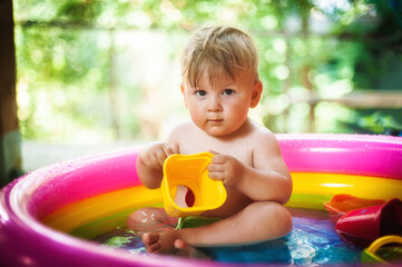 A cute little baby boy is playing with toys while bathing in a little colorful wading pool. Summer time. Joy and happiness concept. Love and family emotion