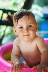 A cute little baby boy is playing with toys while bathing in a little colorful wading pool. Summer time. Joy and happiness concept. Love and family emotion