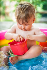 A cute little baby boy is playing with toys while bathing in a little colorful wading pool. Summer time. Joy and happiness concept. Love and family emotion