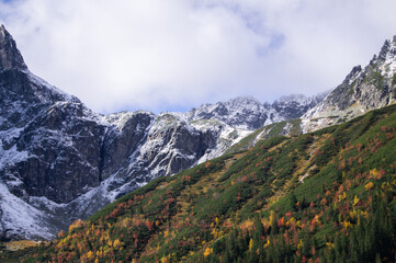 Stunning landscape of High Tatras, Poland. Snow-covered peaks juxtaposed against a lush forest adorned in autumn colors. A vivid display of nature's contrasts, offering tranquility and awe.