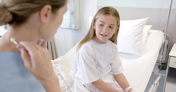 Caucasian female doctor using stethoscope on chest of girl patient on hospital bed, slow motion