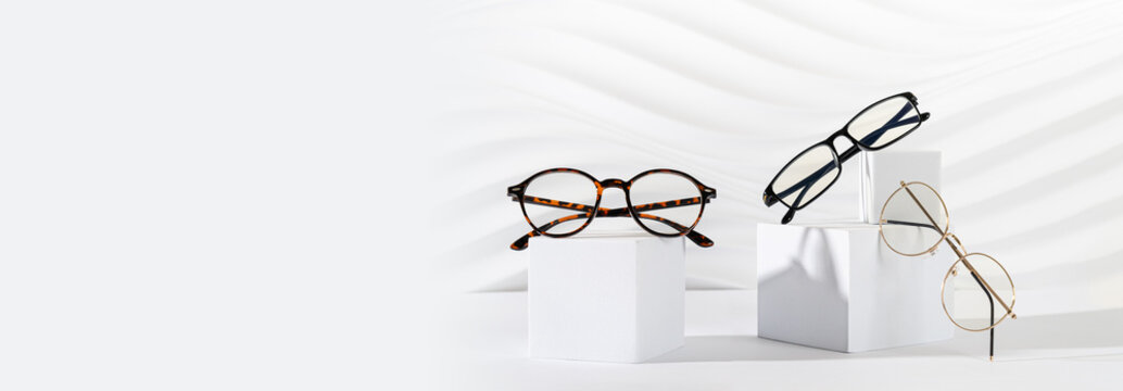 Glasses sale banner. Optic store sale-out offer. Trendy plastic and metallic frame glasses on a podium on white background. Copy space. For banner, web line. Optic store discount, eyewear promotion