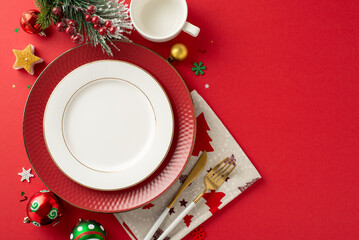 Top view of sophisticated New Year's family dinner table arrangement. Gold cutlery, cup, baubles, candle, and holiday embellishments on red background with open space for text or promotional messages
