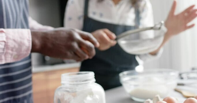 Biracial couple wearing aprons and baking in kitchen, slow motion