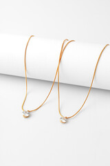 Two golden necklaces with diamond pendant on paper background