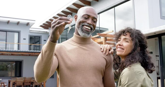 Portrait of happy biracial couple embracing and holding keys at new house, slow motion