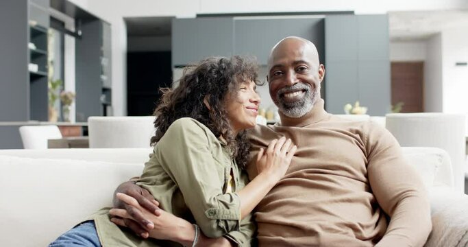Portrait of happy biracial couple embracing and sitting on couch at home, slow motion