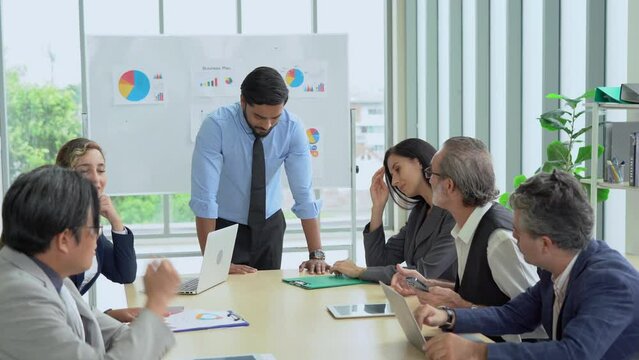 Young indian business manager standing and presenting to group of diversity colleagues in front of white board in meeting at boardroom in office . leader listen and answer questions coworker asking