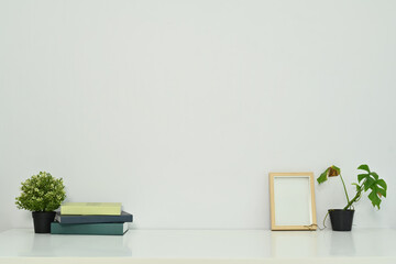 Minimal workplace with books, coffee cup, photo frame and potted plants on table against a clean...