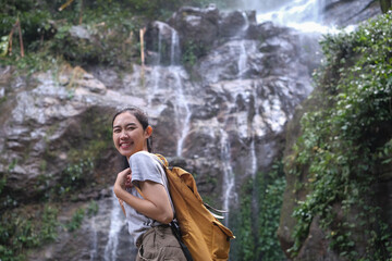 Portrait of smiling female adventurous with backpack standing in front of tropical waterfall