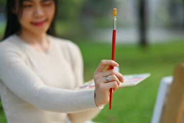 Select focus on female artist holding paintbrush while painting picture in the green park